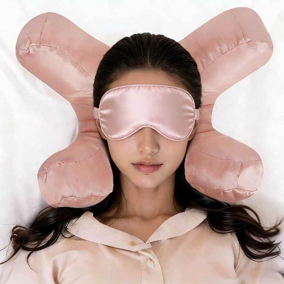 Model wearing the matching pink satin eye mask while resting her head on the anti-wrinkle face pillow