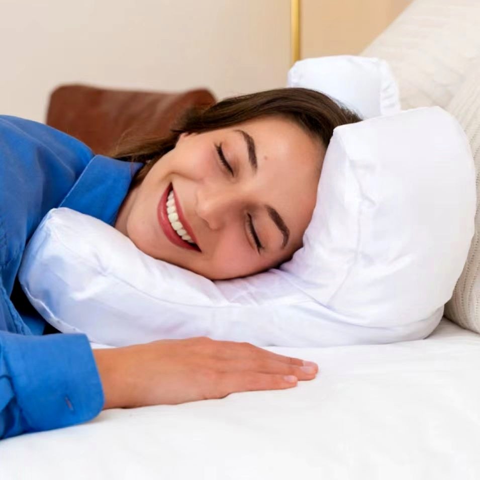 Woman side-sleeping on the white satin face pillow, smiling with her cheek resting in the hollow